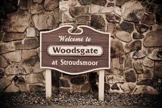 Wooden sign against a stone wall reads Welcome to Woodsgate at Stroudsmoor