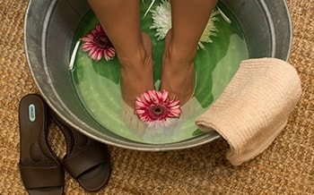 Close up of feet in a spa treatment. The water is green with flowers floating.