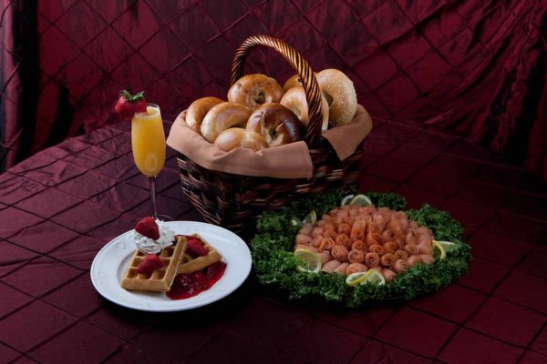 A basket with bagels, a plate with strawberry topped waffles, and a plate of deli meat