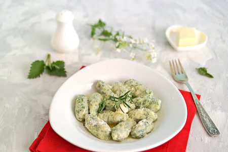 Gnocchi or dumplings with nettle or spinach on a white plate on a light gray background. Served with butter and parmesan cheese. Italian food. Selective focus