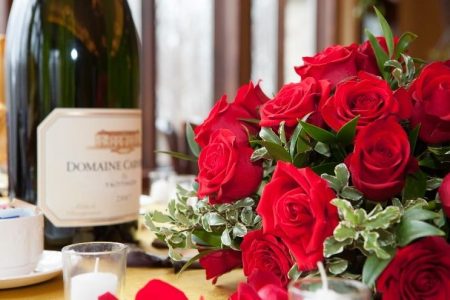 Close up of red roses with a bottle of champagne in the background